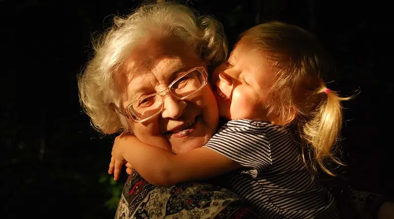 A blonde toddler hugging an elderly lady with glasses