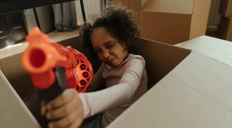 Girl with a toy gun hiding in a moving box