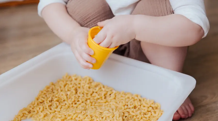 A child plays with dry macaroni in a sensory tray
