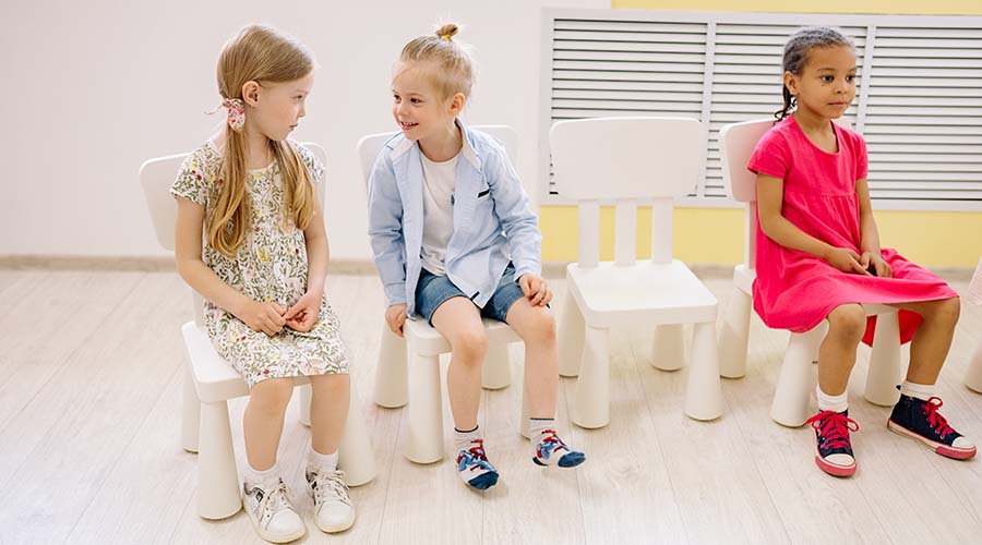 A photo of three girls sitting on white chairs in an Early Years classroom.