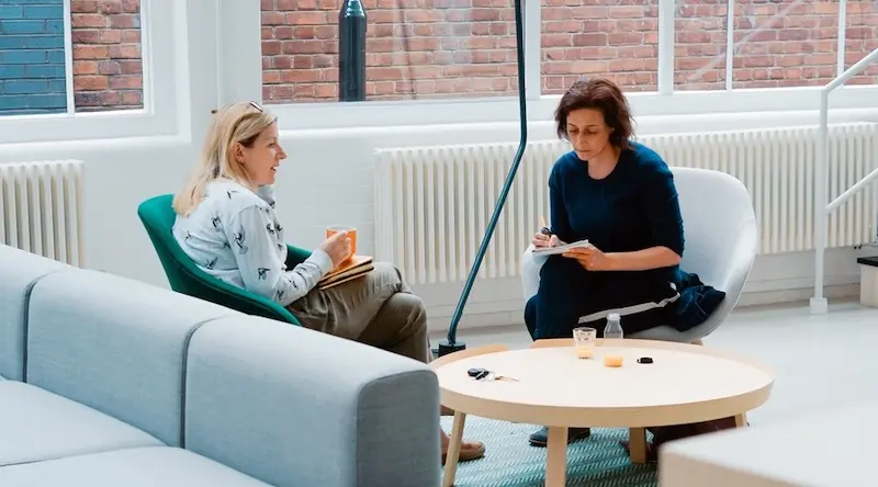 Two women in a big open space talking and writing notes