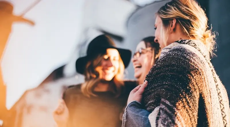 3 women laughing together at sunset