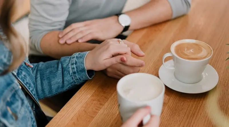 Two people having coffee and holding hands