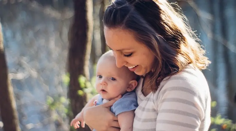 Smiling woman holding a baby outdoors