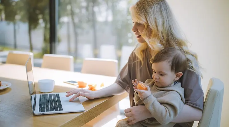 Woman holding a toddler while working on a computer