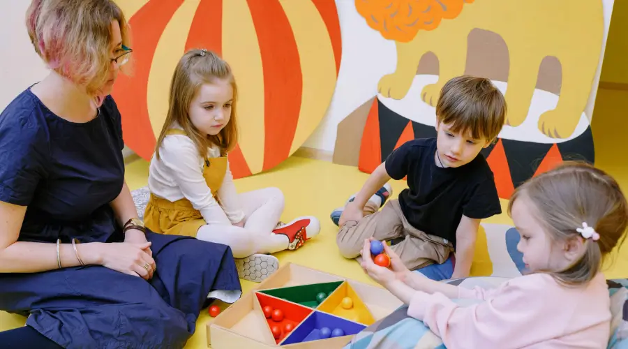 preschool teacher and children playing with balls on the floor