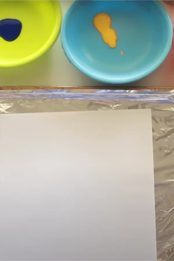 Paper laid on a table with bowls of paint for children's art