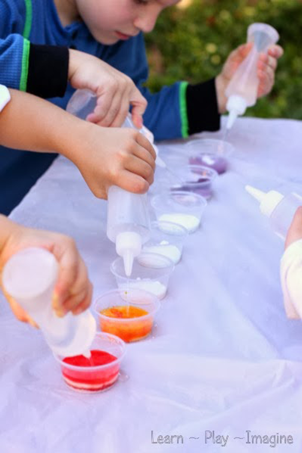 A row of shallow plastic bowls have vinegar squirted into them by several children.