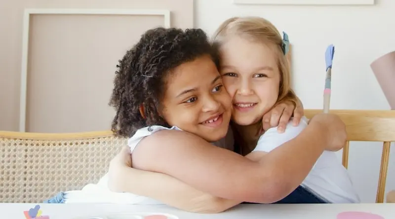 Two children sit at a table and hug