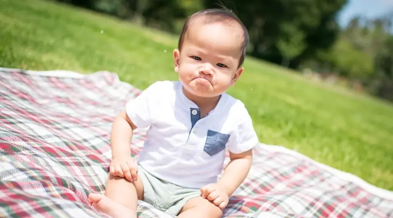 A pouting child sits on a blanket