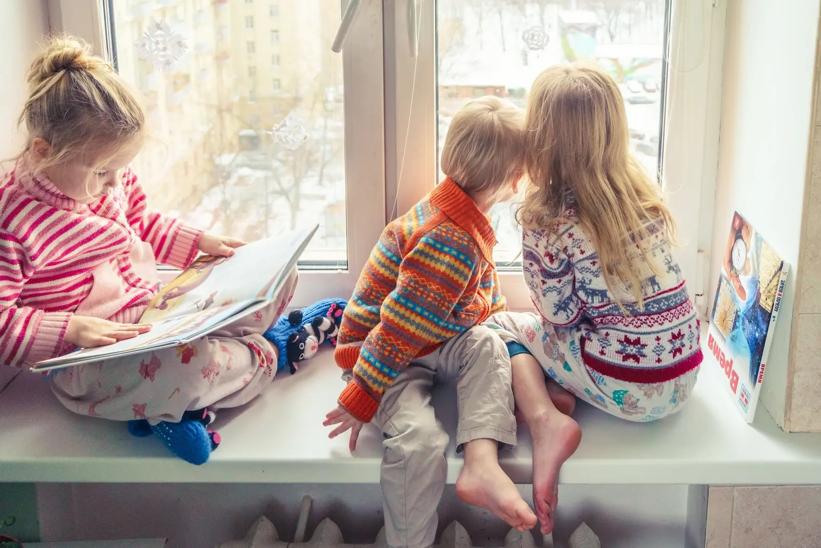 Kinder in Weihnachtspullovern schauen durchs Fenster