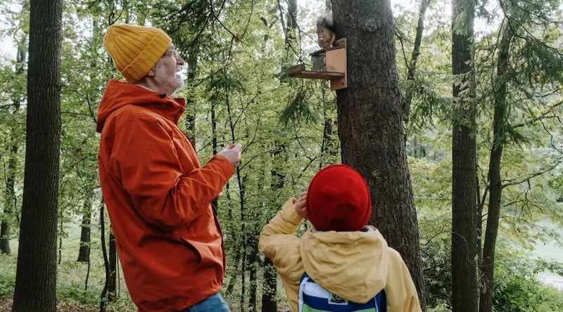 Old man with a child observing a squirrel in a forest
