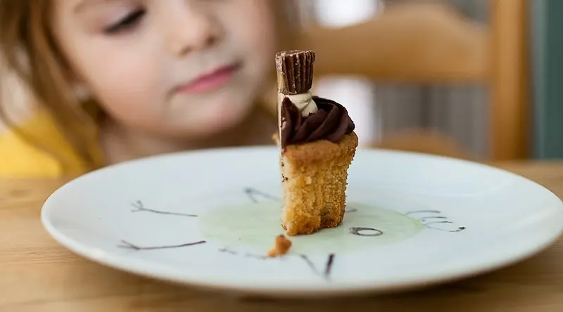 An early years child looks at a slice of cake being served in their nursery.