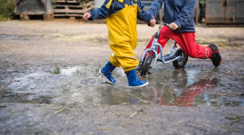 Two children, one on a bike,, one running, play in the puddles and mud.