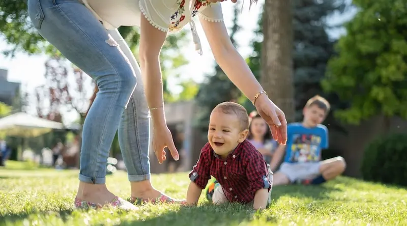 Woman picking up a smiling toddler on green grass