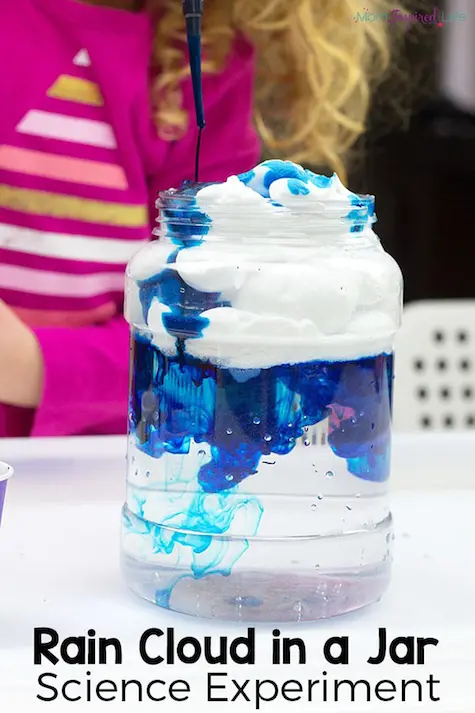 A glass beaker containging shaving foam on top of water. Coloured paint is being dripped through it.