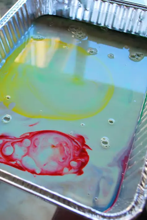 A silver tray of milk with coloured paint swirled into it.