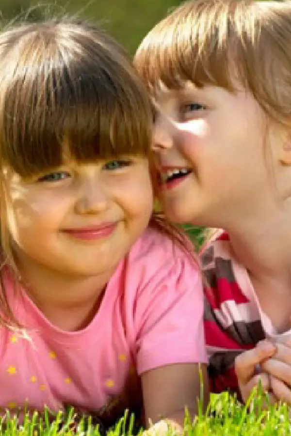 One girl talking on the ear of another