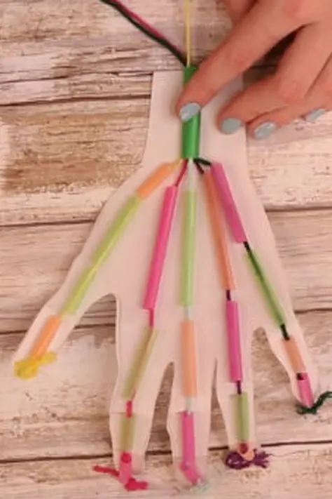 A hand-shaped piece of paper with small pieces of drinking straws taped to it. There is string threaded through the paper.