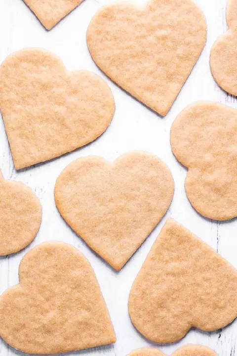 Heart-shaped cookies arranged on a rustic white wooden surface. The golden-brown cookies convey a warm, homemade feel, perfect for festive or romantic occasions.