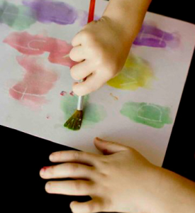 A child colouring white piece of paper with paint.