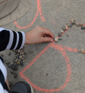A kid tracing letter B with small stones.