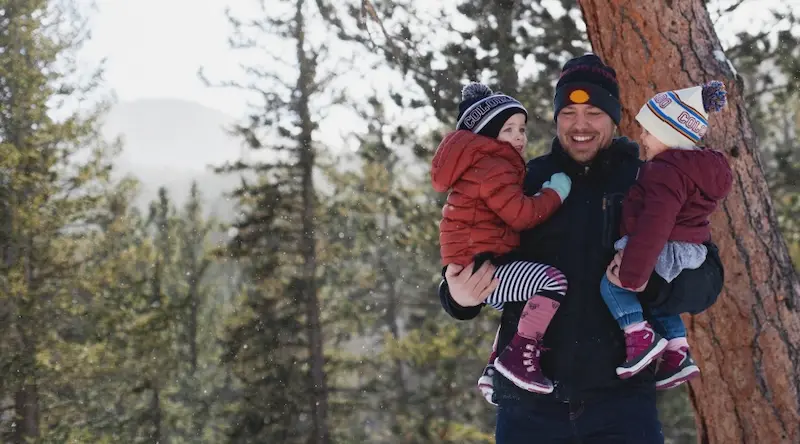 Father holding two kids in his arms laughing in the forest