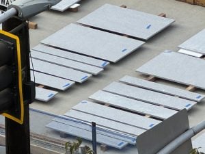 Stacks of light gray concrete slabs with blue corner tape, arranged on pallets in a construction yard beside equipment
