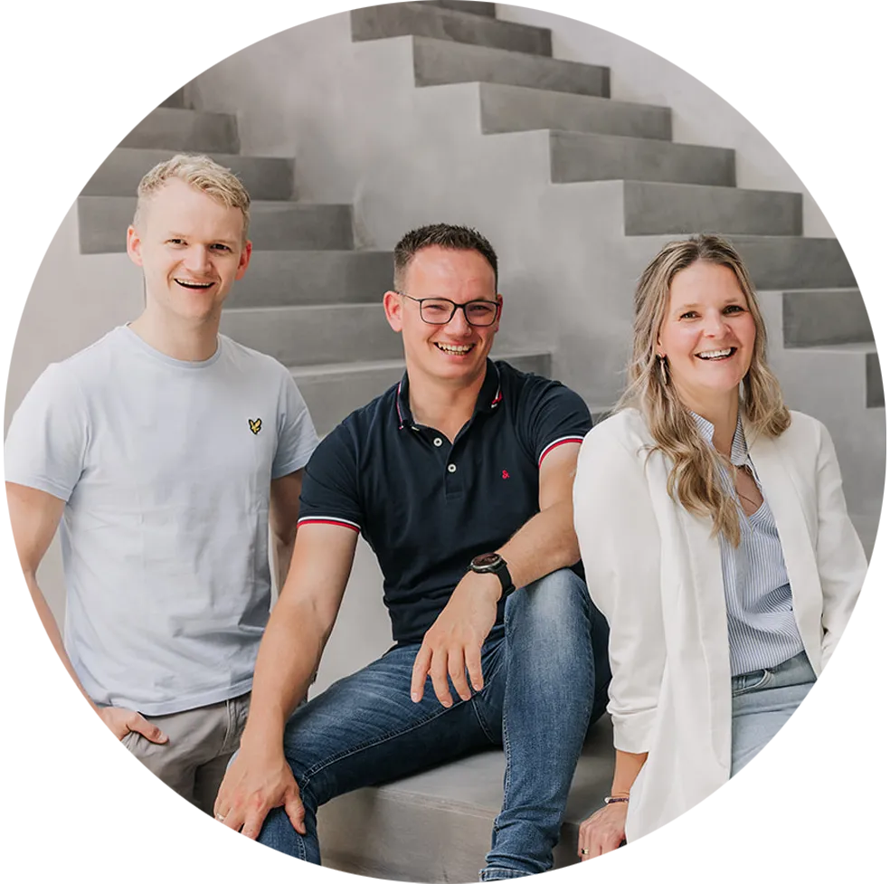 A smiling group of three people sitting and standing on gray concrete stairs, two men and one woman dressed casually.
