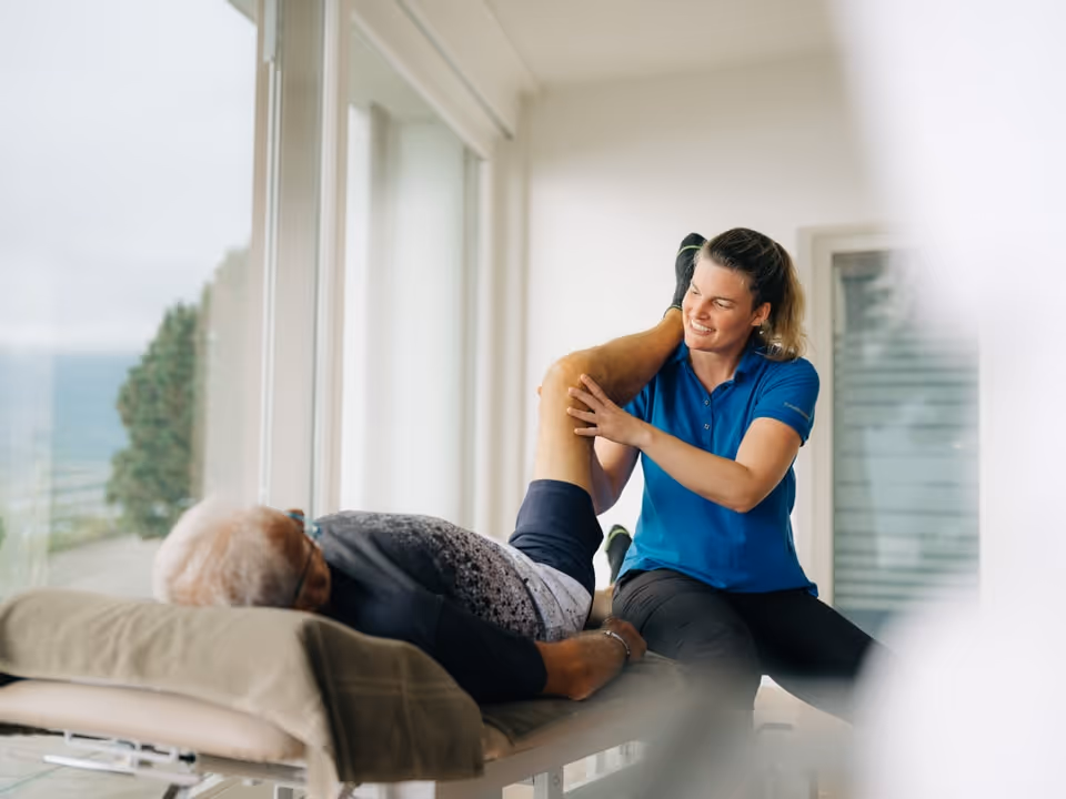 Physiotherapeutin bewegt Bein eines liegenden Patienten