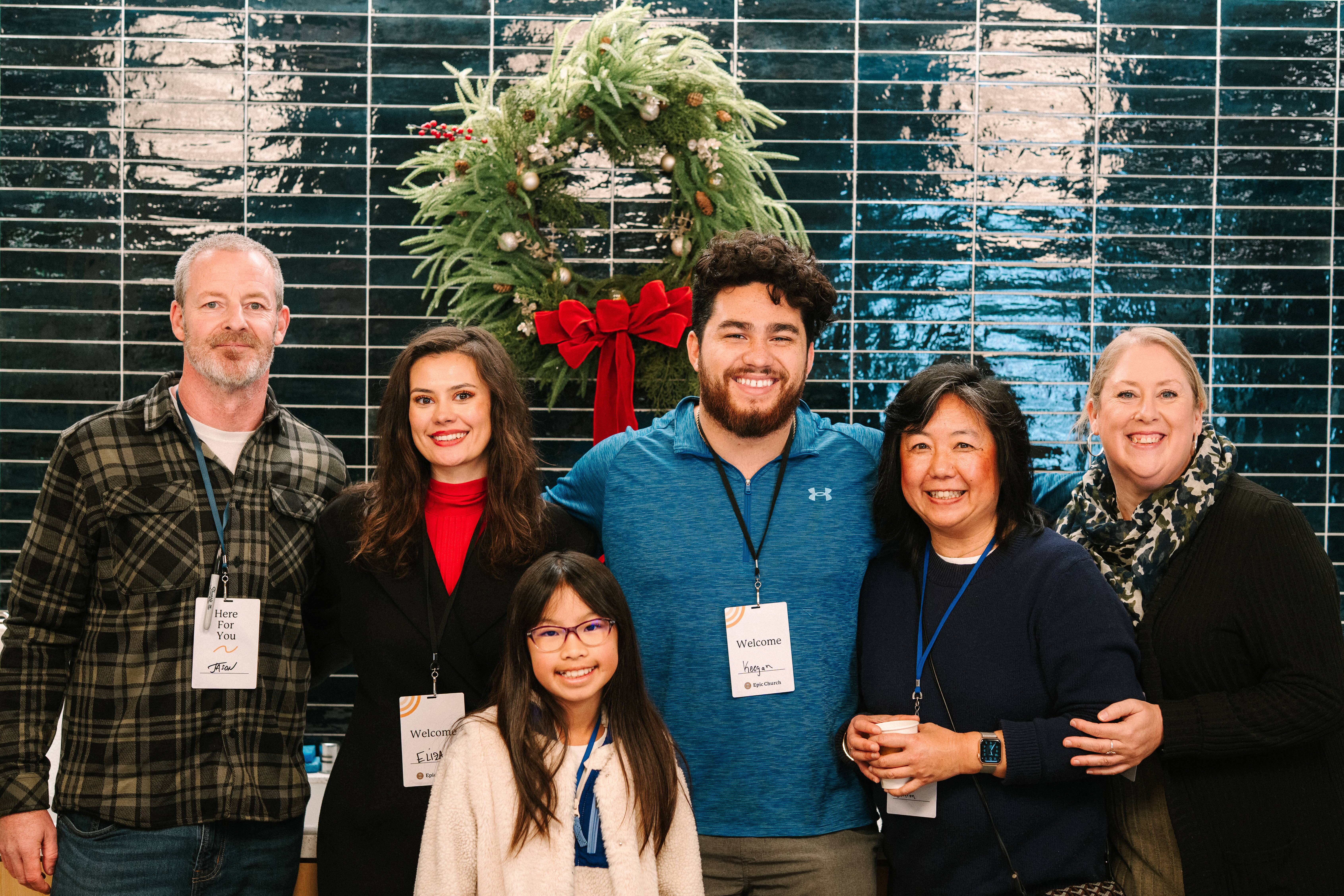 Three people smiling outdoors, including a young man with a backpack, an older woman in a blue shirt, and a woman wearing glasses and a floral dress.