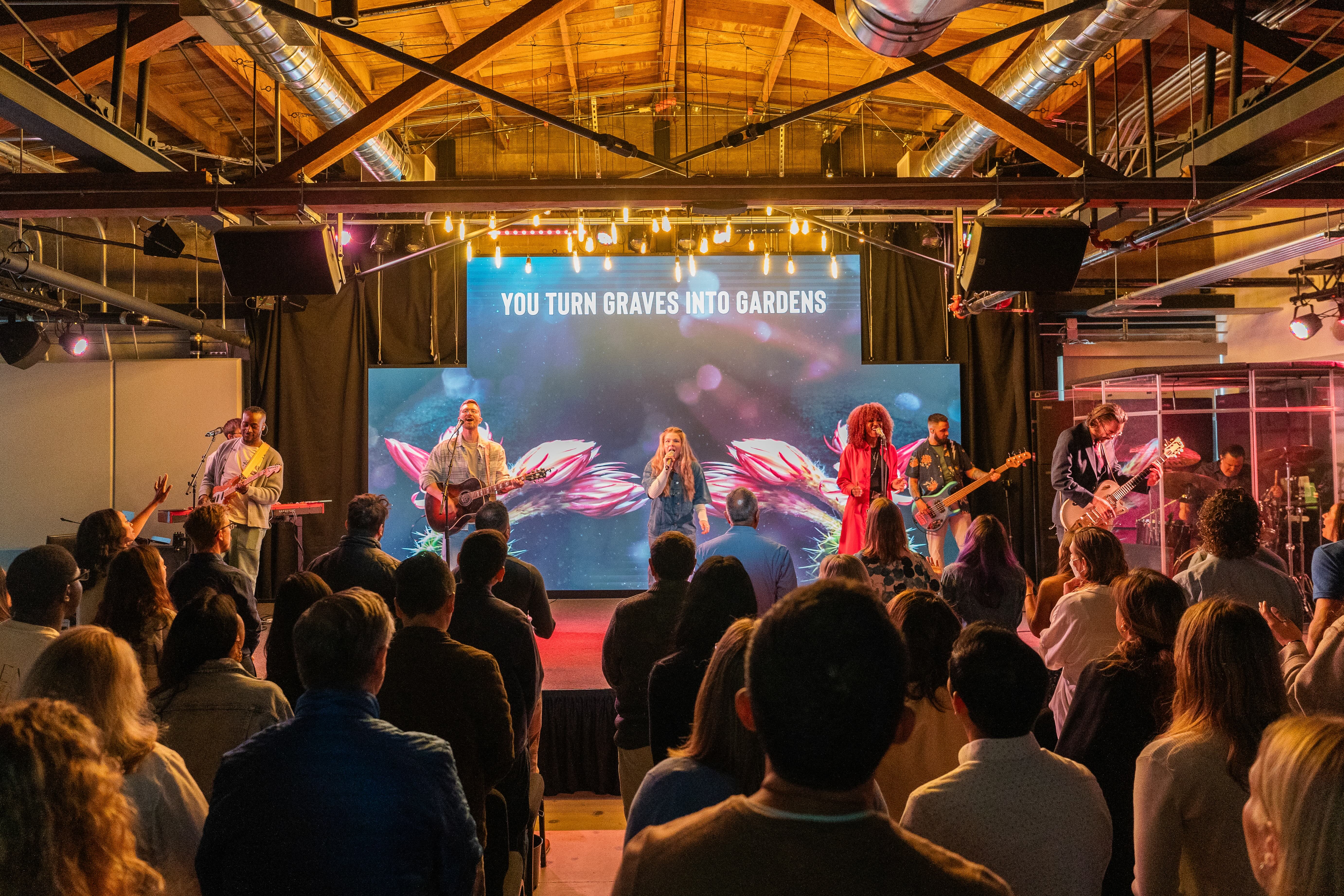 Three people smiling outdoors, including a young man with a backpack, an older woman in a blue shirt, and a woman wearing glasses and a floral dress.