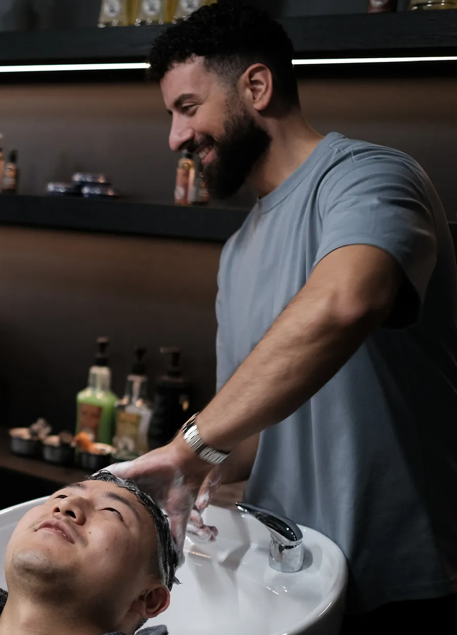 Man die glimlachend iemands haar wast in een kapsalon boven een wasbak.