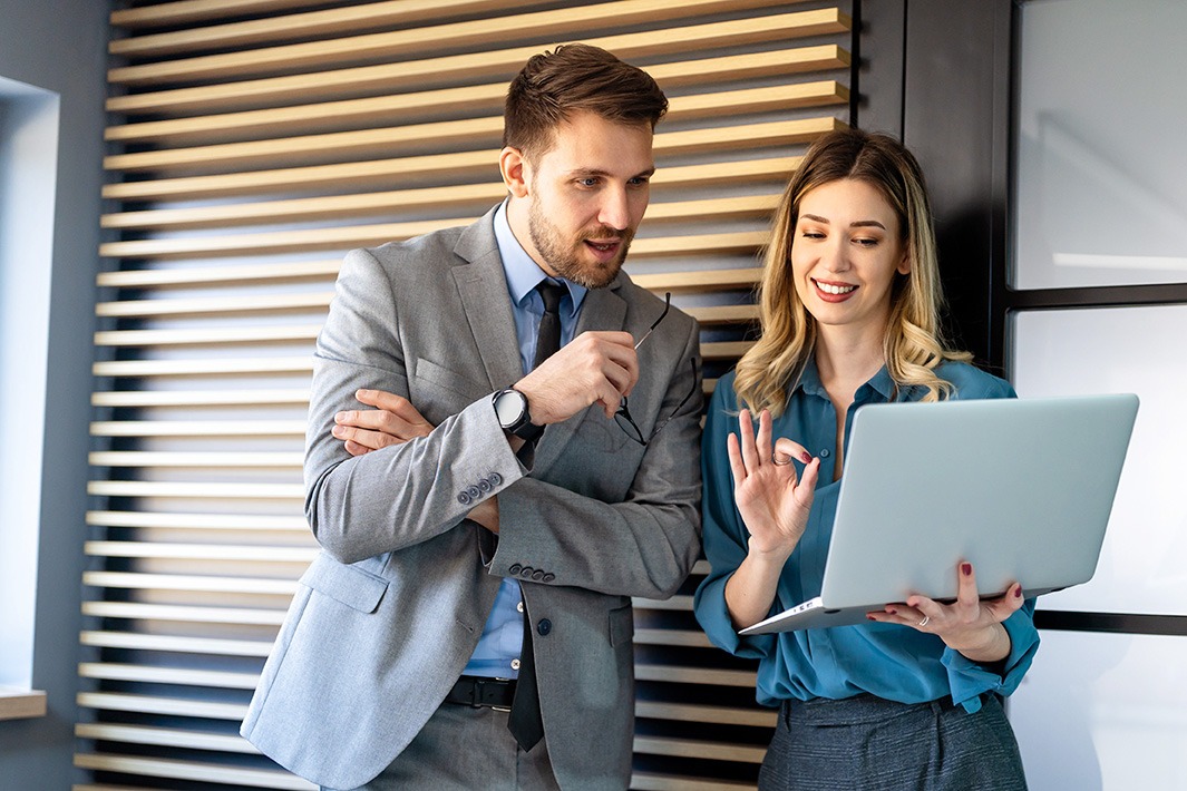 A male and female coworker looking at a laptop screen and collaborating.