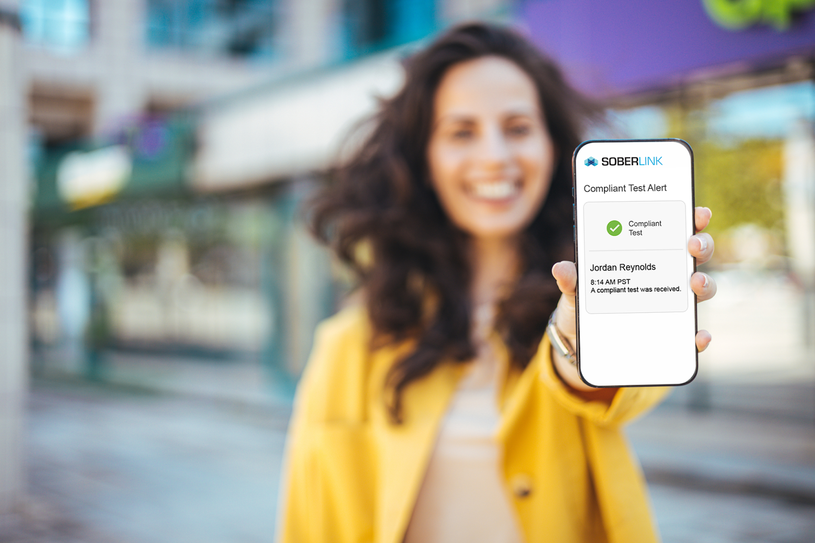 A woman showing her phone screen with a Soberlink compliant test alert.