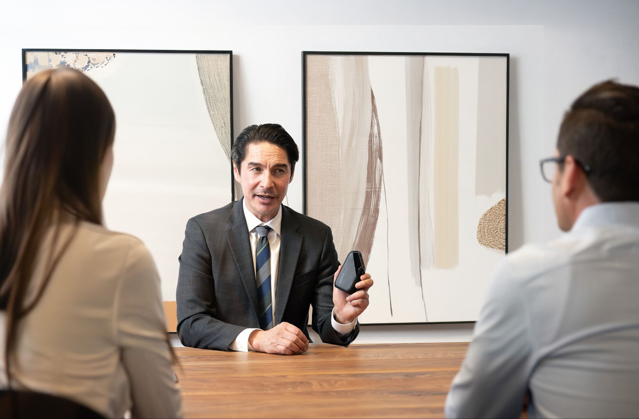 A man presenting the Soberlink device to a man and woman.