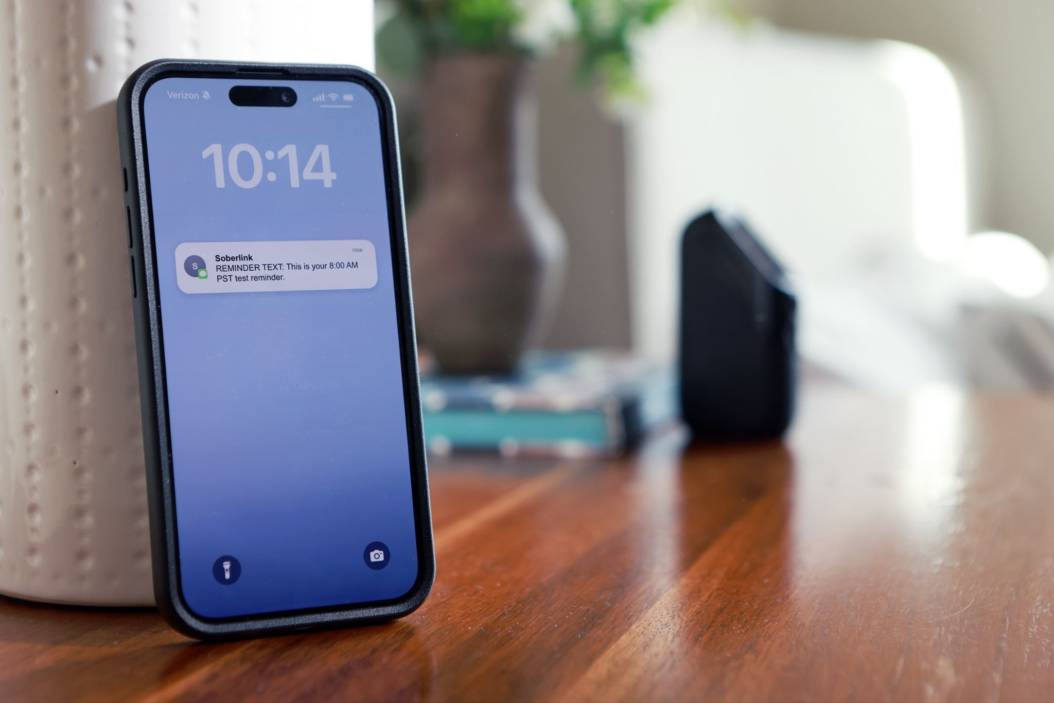 A phone that is displaying a Soberlink reminder text with a Soberlink device in the background.