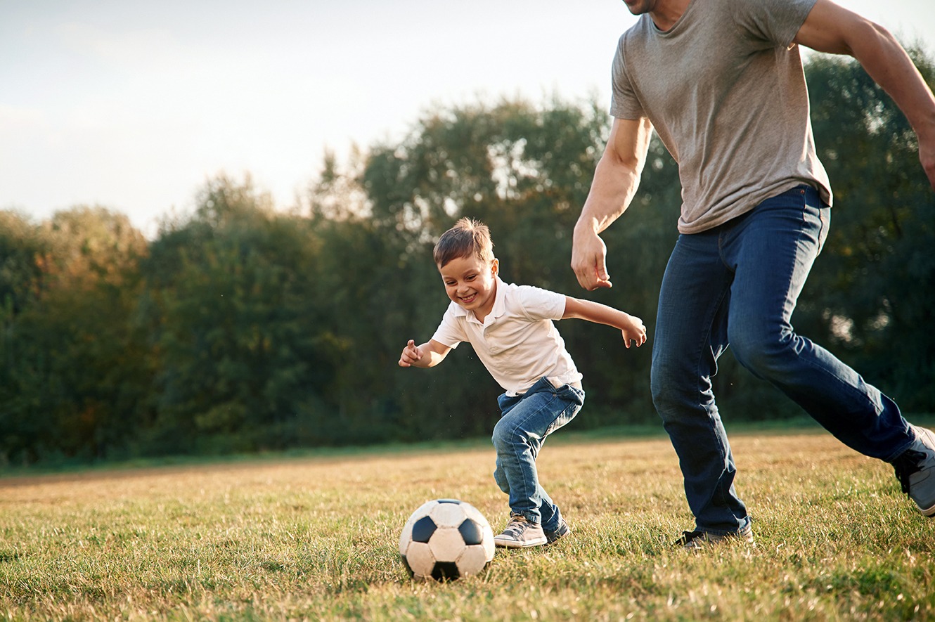 A father and son playing soccer.