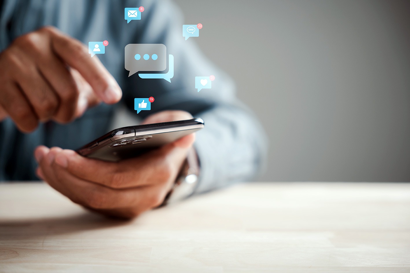 A close-up of hands holding a smartphone, with icons for messages, comments, likes, and social notifications floating above the screen, representing app engagement and community features.