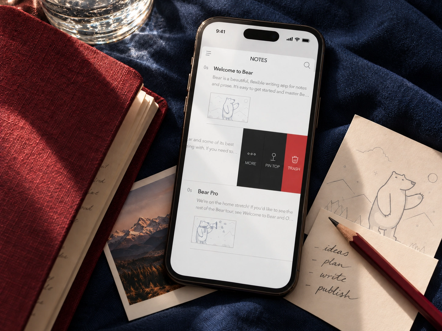 Bear notes app on a phone with a red notebook and sketches on navy fabric.