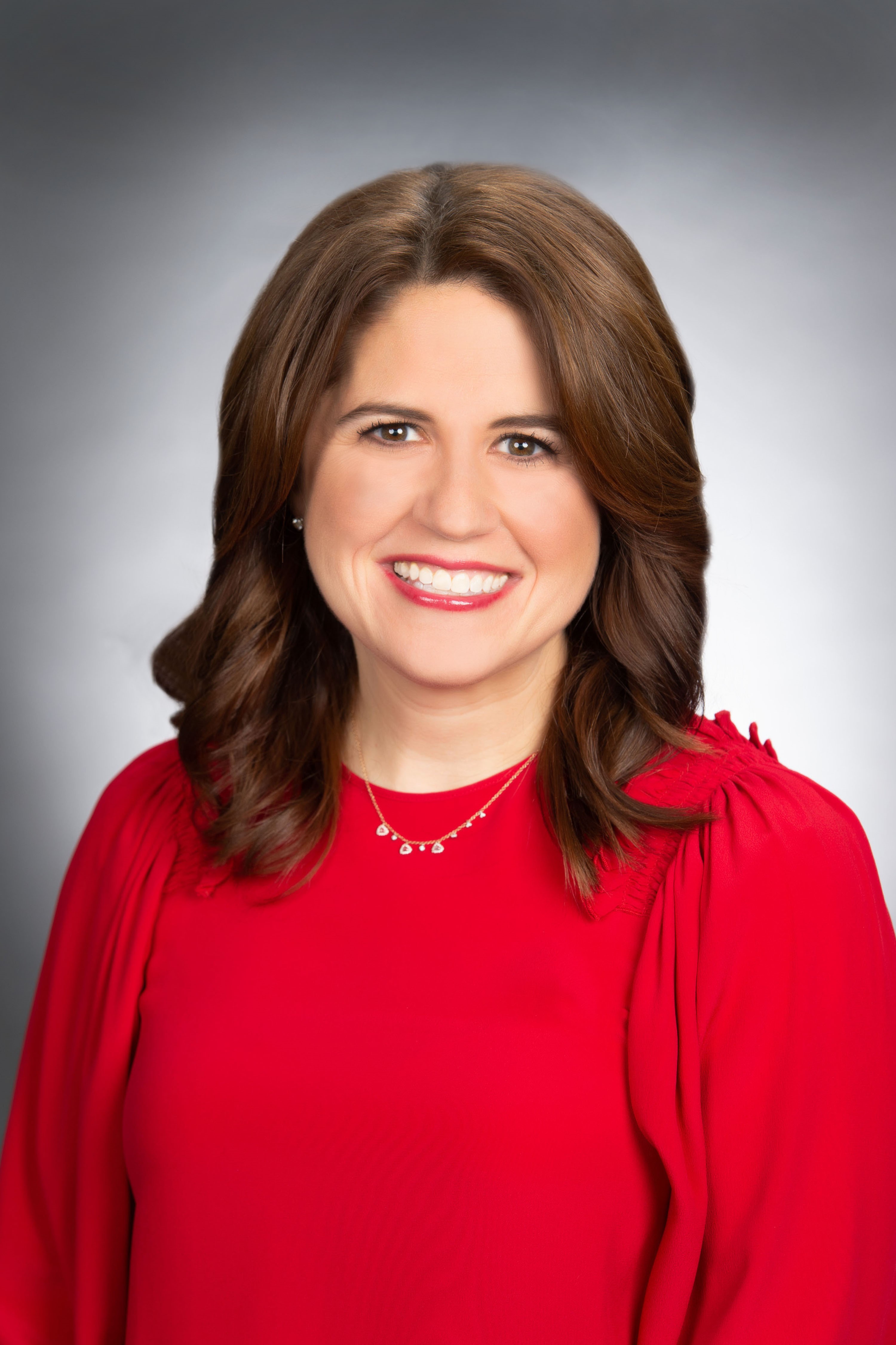 Woman in red shirt, with brown shoulder length hair, smiles brightly at camera