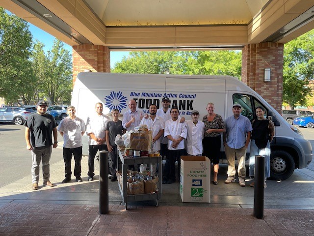 A box of food items and a group of people stand in front of a white van.