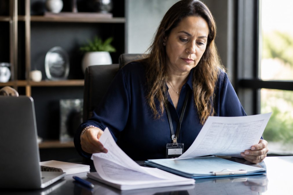 Practice administrator reviewing HIPAA compliant marketing software pricing documentation and compliance checklist at desk with laptop and security badge visible