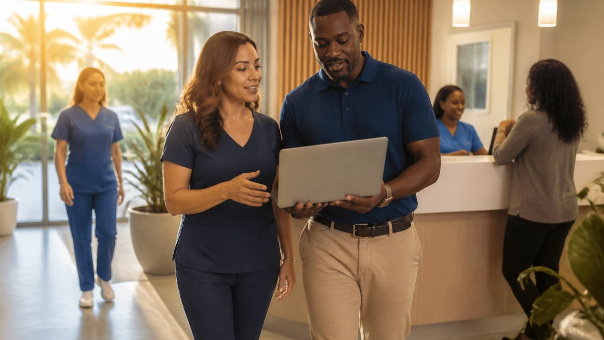 A clinic administrator and marketing lead reviewing Google Business Profile insights on a laptop in a bright clinic office, with a front desk visible in the background