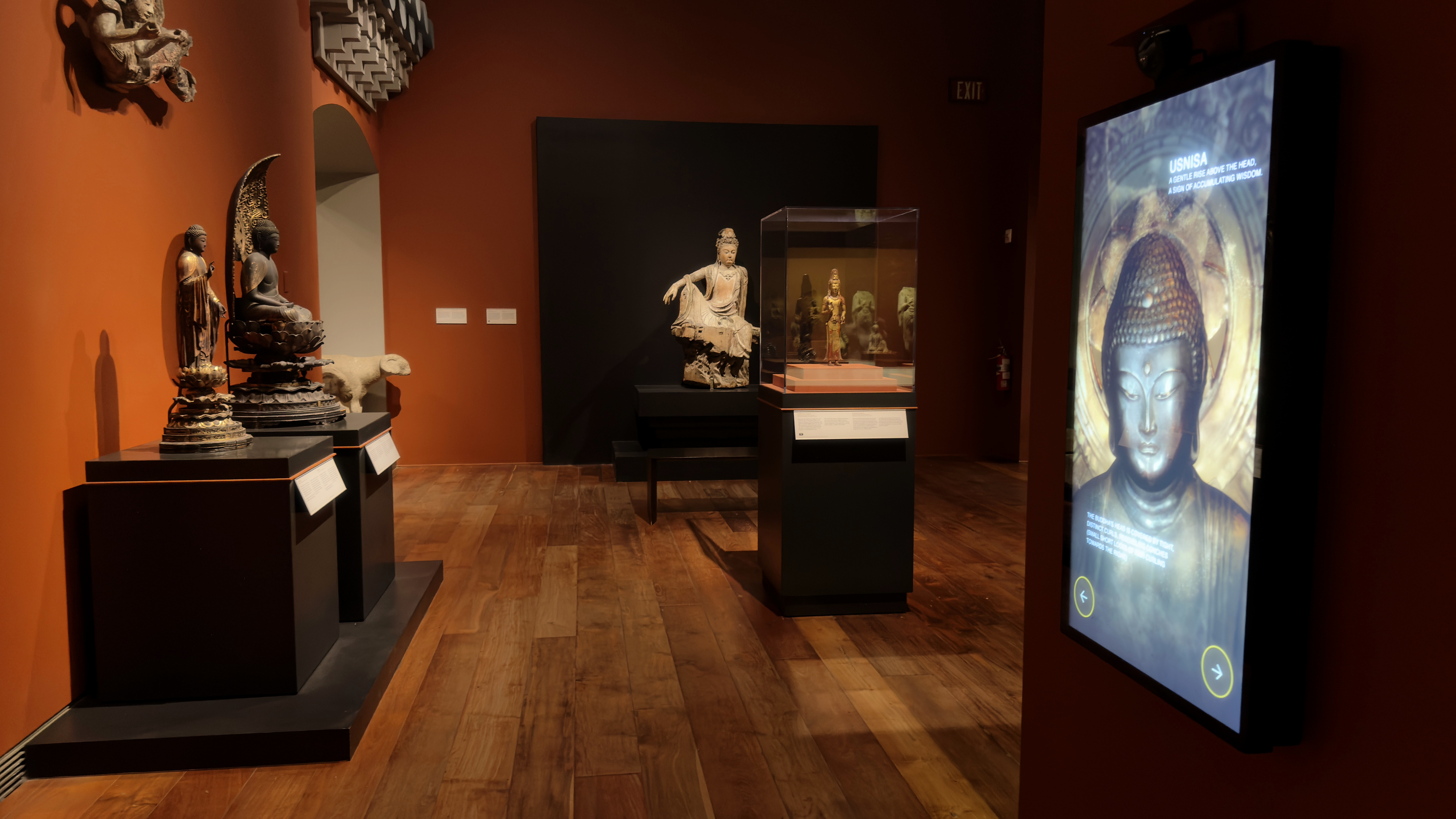 Wide view of the Temple Room: the station's Learn mode in the foreground, the collection of Buddhist sculptures it interprets across the gallery.
