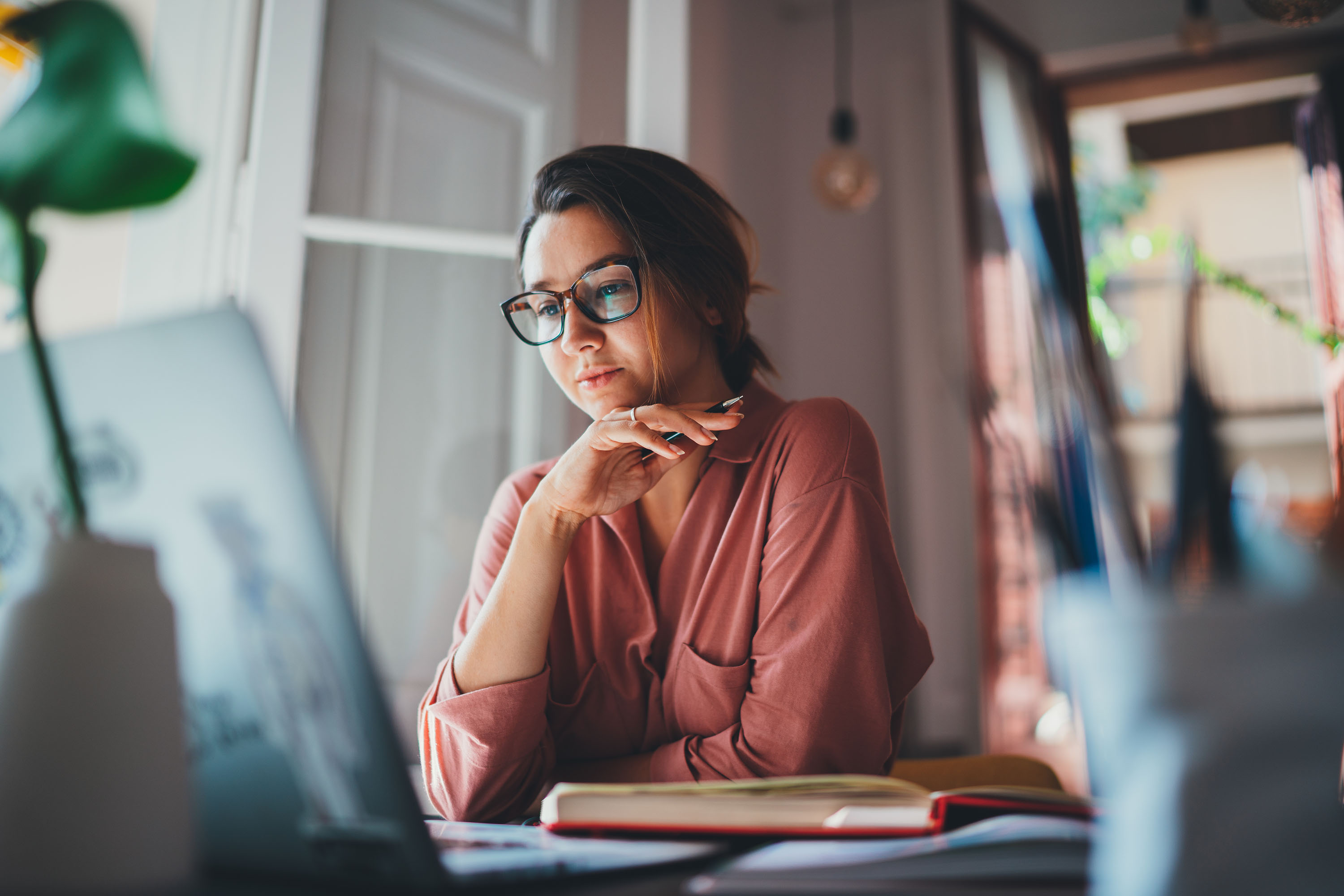 Lady with trendy glasses sits at her home workspace with a laptop.