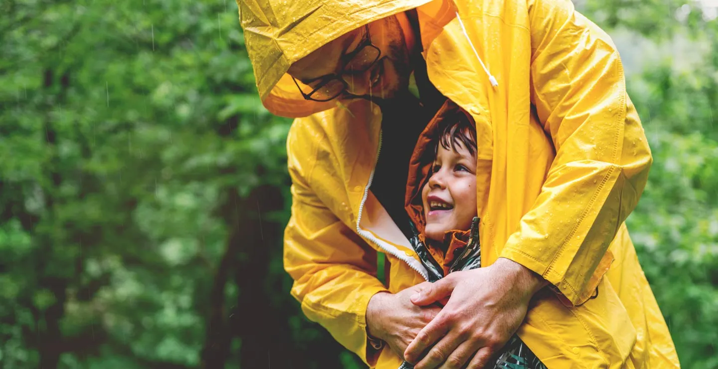 father wearing yellow jacket and covering his child from the rain
