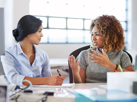 Duas mulheres conversando com um relatório em mãos.