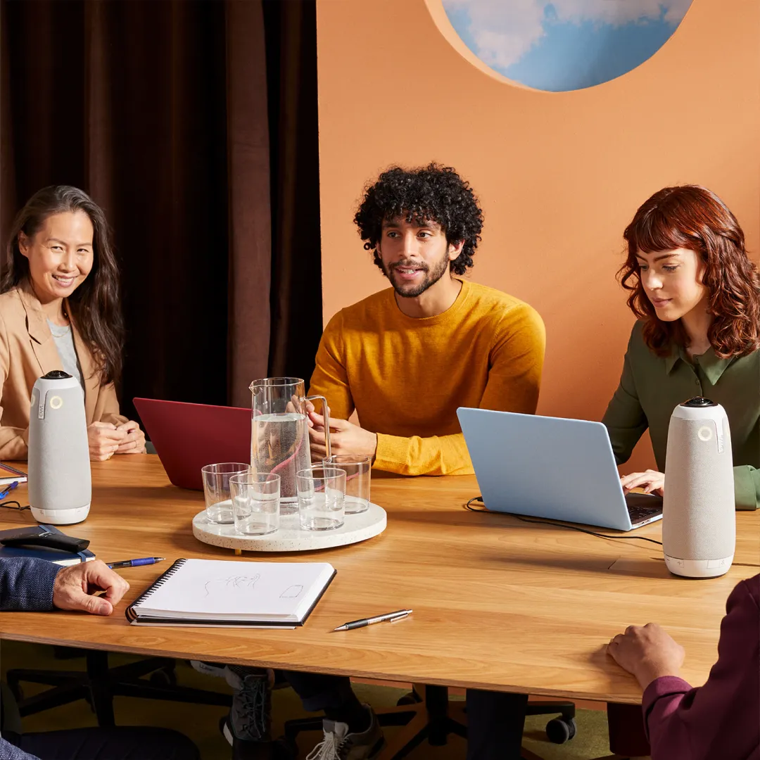 Four people in a business meeting around a table, with two Meeting Owl devices placed on the table