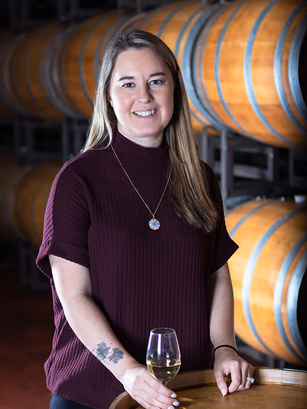 Sara Varela standing in a barrel room with her hand on a glass of white wine